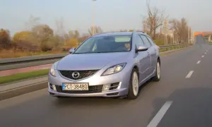 Fioletowa Mazda 6 GH jedzie po drodze. Jej żarówki świecą jasno, oświetlając trasę.