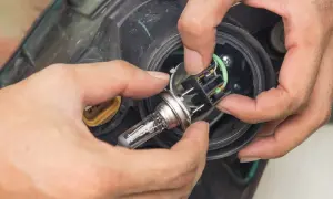 Wymiana żarówki H7 w Mazda 5. Dłonie montują nową żarówkę w reflektorze.