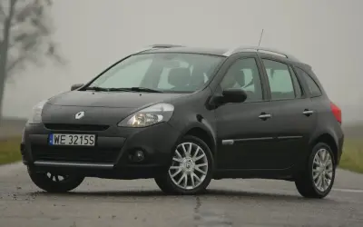 Ciemny Renault Clio 3 na mokrej drodze, widoczne przednie żarówki.