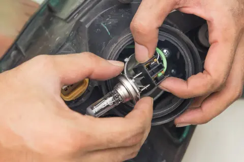 Wymiana żarówki H7 w Mazda 5. Dłonie montują nową żarówkę w reflektorze.