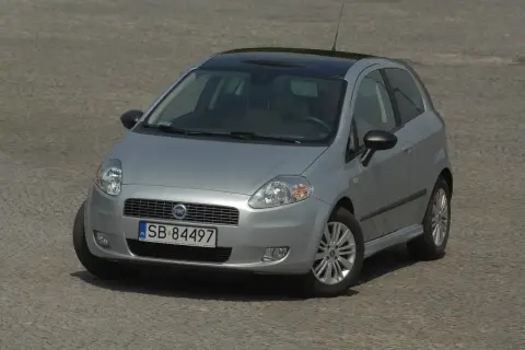 Srebrny Fiat Grande Punto z czarnym dachem i nowymi żarówkami, gotowy do jazdy po brukowanej nawierzchni.