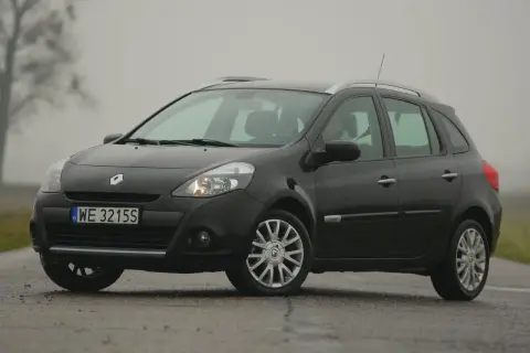 Ciemny Renault Clio 3 na mokrej drodze, widoczne przednie żarówki.