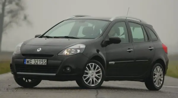 Ciemny Renault Clio 3 na mokrej drodze, widoczne przednie żarówki.