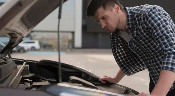 Mężczyzna pochyla się nad otwartą maską Hyundai i20, przygotowując się do wymiany żarówki mijania.