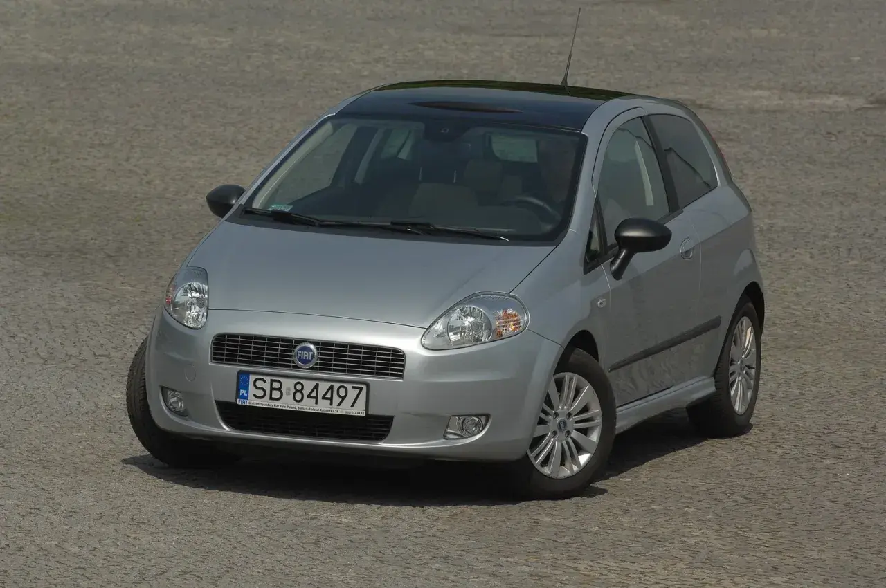 Srebrny Fiat Grande Punto z czarnym dachem i nowymi żarówkami, gotowy do jazdy po brukowanej nawierzchni.