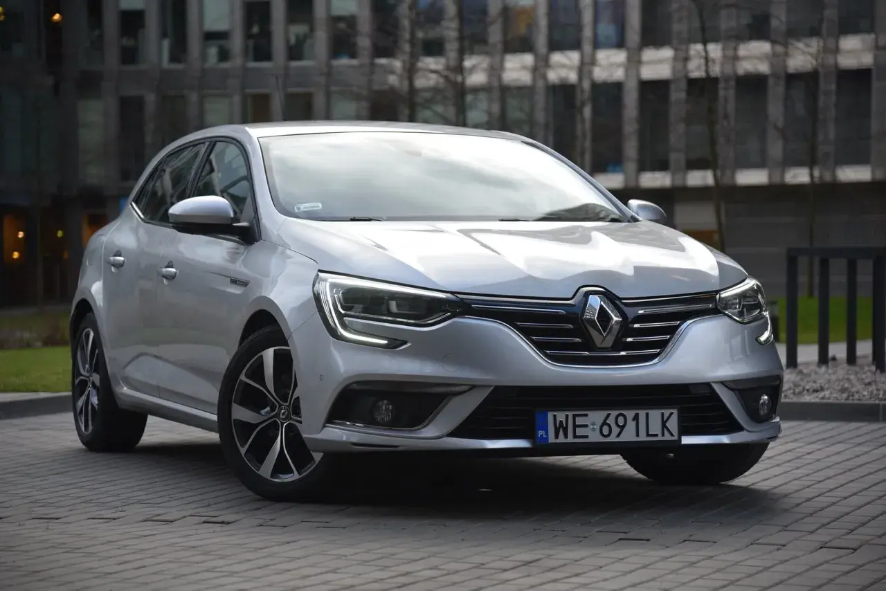 Srebrny Renault Megane 4 z nowoczesnymi żarówkami z przodu, zaparkowany przed budynkiem.