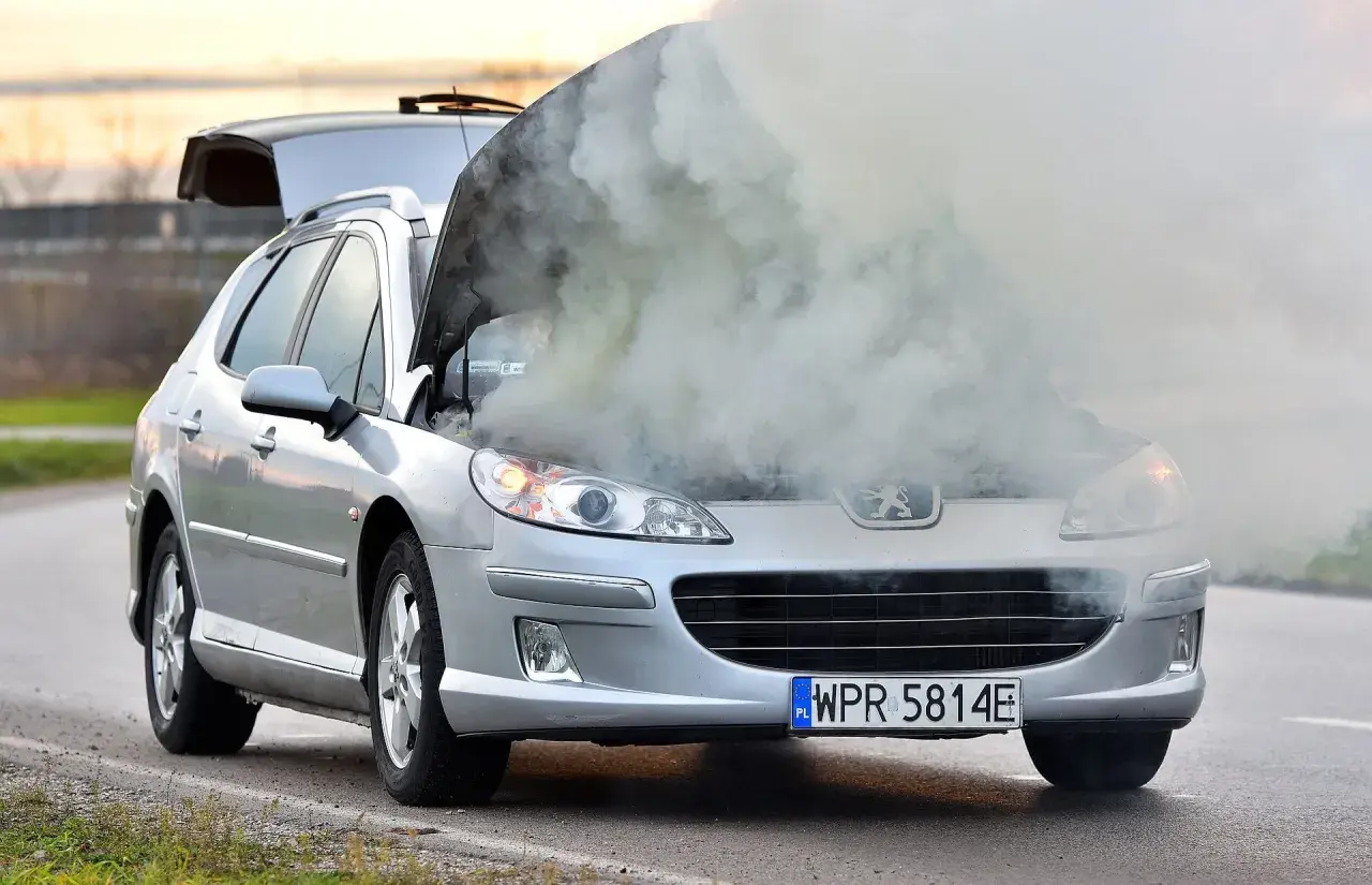 Srebrny Peugeot z otwartą maską i kłębami dymu. Chyba ten rozbiegany diesel potrzebuje pomocy.