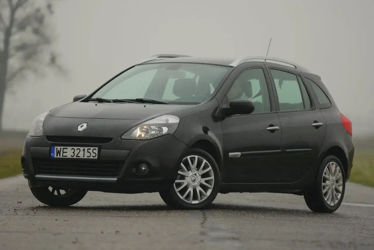 Ciemny Renault Clio 3 na mokrej drodze, widoczne przednie żarówki.