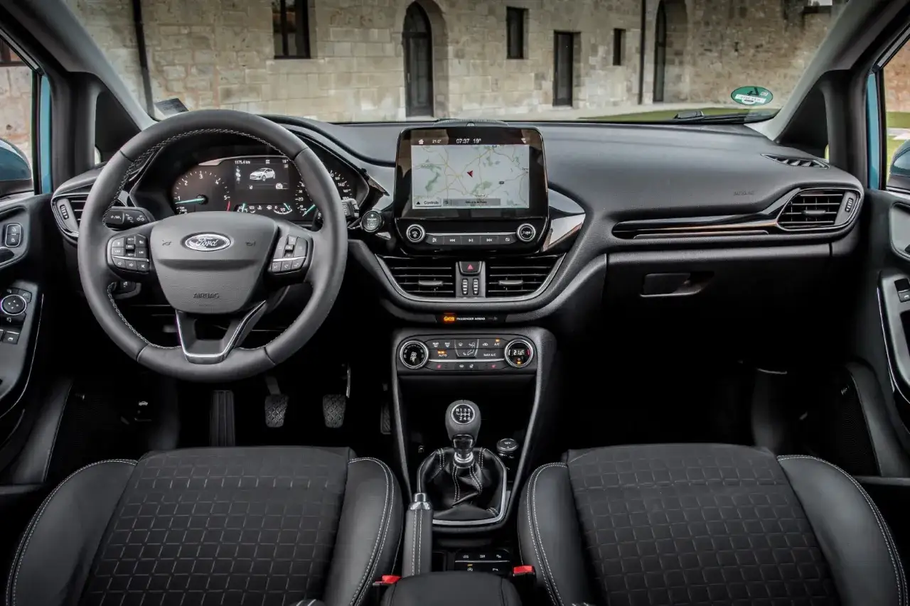Wnętrze Ford Fiesta MK9: kierownica, ekran nawigacji, dźwignia zmiany bieg&oacute;w i czarne fotele.