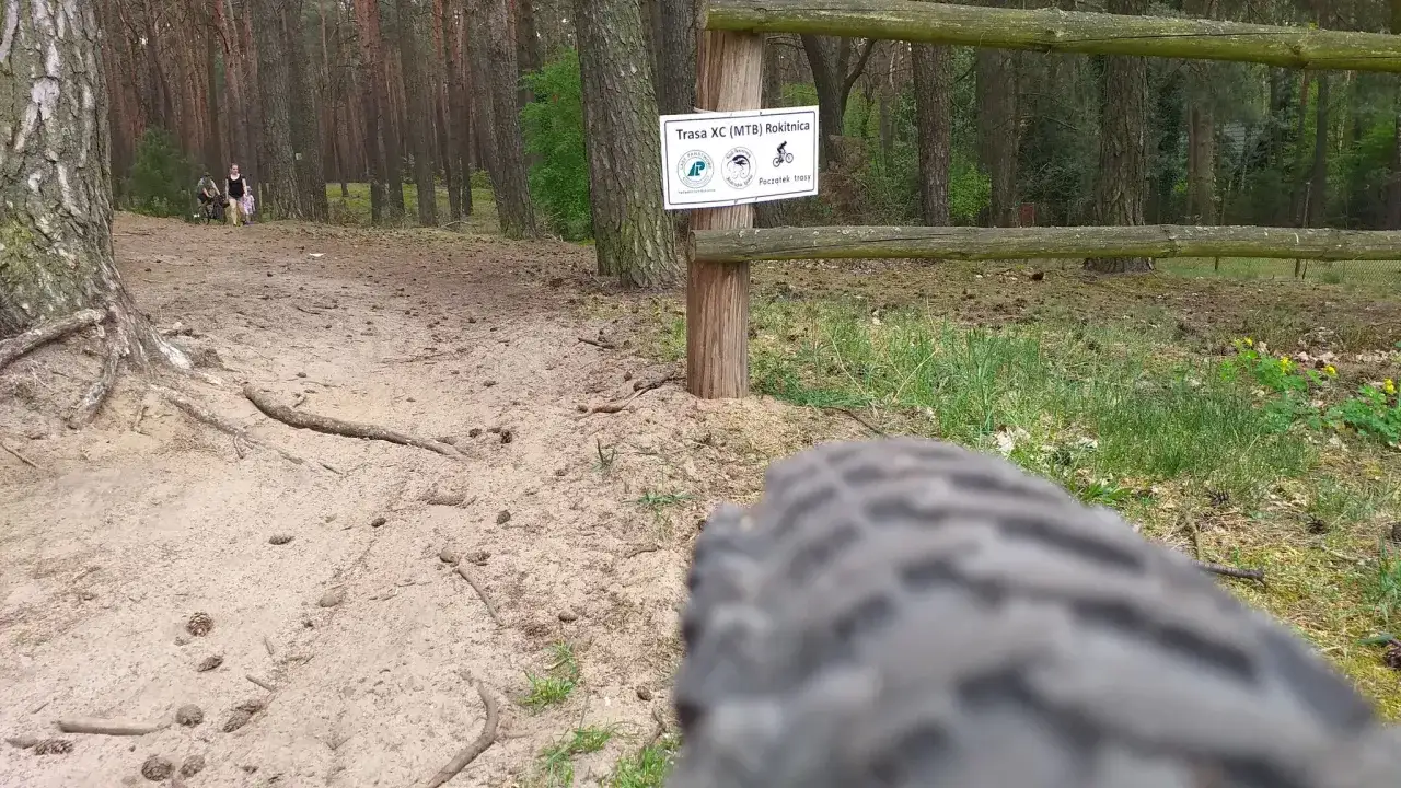 Leśna ścieżka, idealna na rowerowy gravel po łódzku. W tle widać ludzi i tabliczkę