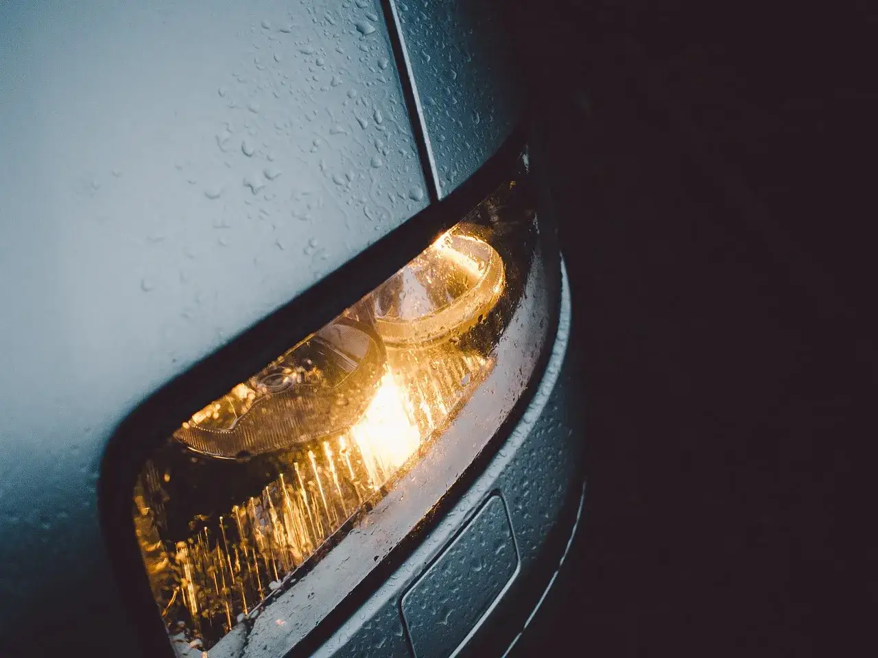 Świecące żarówki przód Peugeot 206 w deszczu. Krople wody na kloszu reflektora.