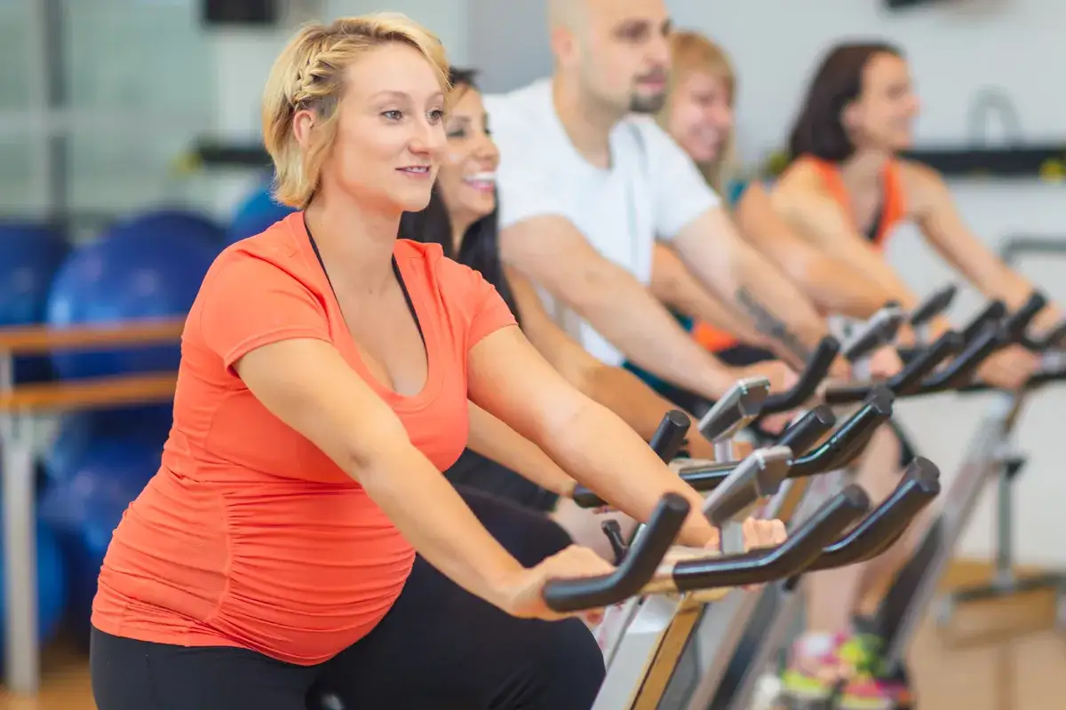 Ciężarna kobieta ćwiczy na rowerku stacjonarnym, pokazując, że czy w ciąży można jeździć na rowerze jest możliwe, gdy jest to bezpieczne.