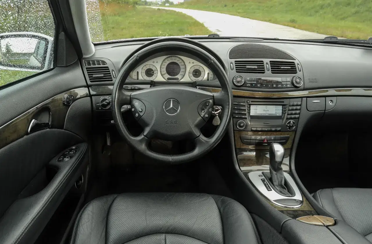 Wnętrze Mercedesa E Klasa 2004 z czarną sk&oacute;rzaną tapicerką, drewnianymi wstawkami i kluczykami w stacyjce.