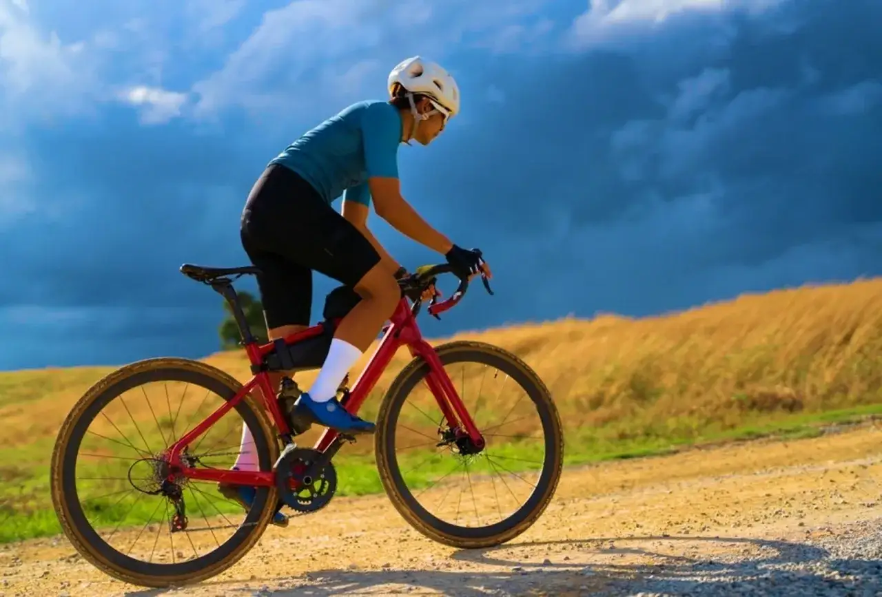 Kobieta w kasku i okularach pokonuje szutrową trasę na czerwonym rowerze gravel.