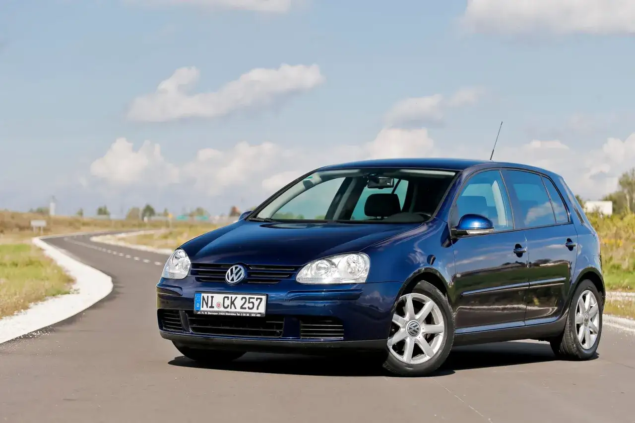 Ciemnoniebieski Volkswagen Golf 5 na tle błękitnego nieba z chmurami. Świetne żarówki w tym modelu!