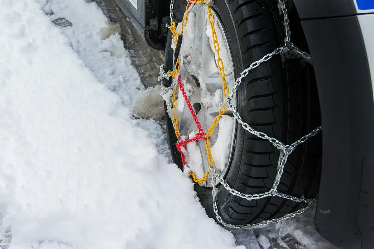 Montaż łańcuchów śniegowych na kole samochodu w zaspie śnieżnej. Metalowe ogniwa zapewniają przyczepność na śliskiej nawierzchni.