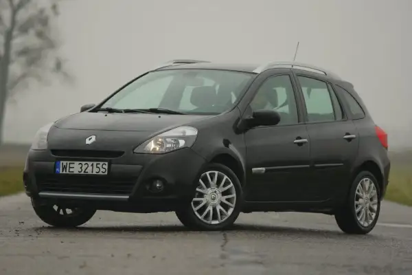 Ciemny Renault Clio 3 na mokrej drodze, widoczne przednie żarówki.