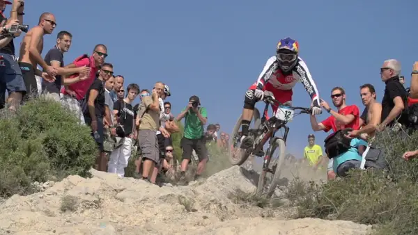 Kolarz w akcji podczas zawodów MTB, otoczony przez widzów i fotografów.